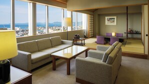Una habitación de hotel moderna con un amplio ventanal que ofrece vistas a la ciudad, un sofá, una mesita y una zona con esterillas de tatami japonesas.