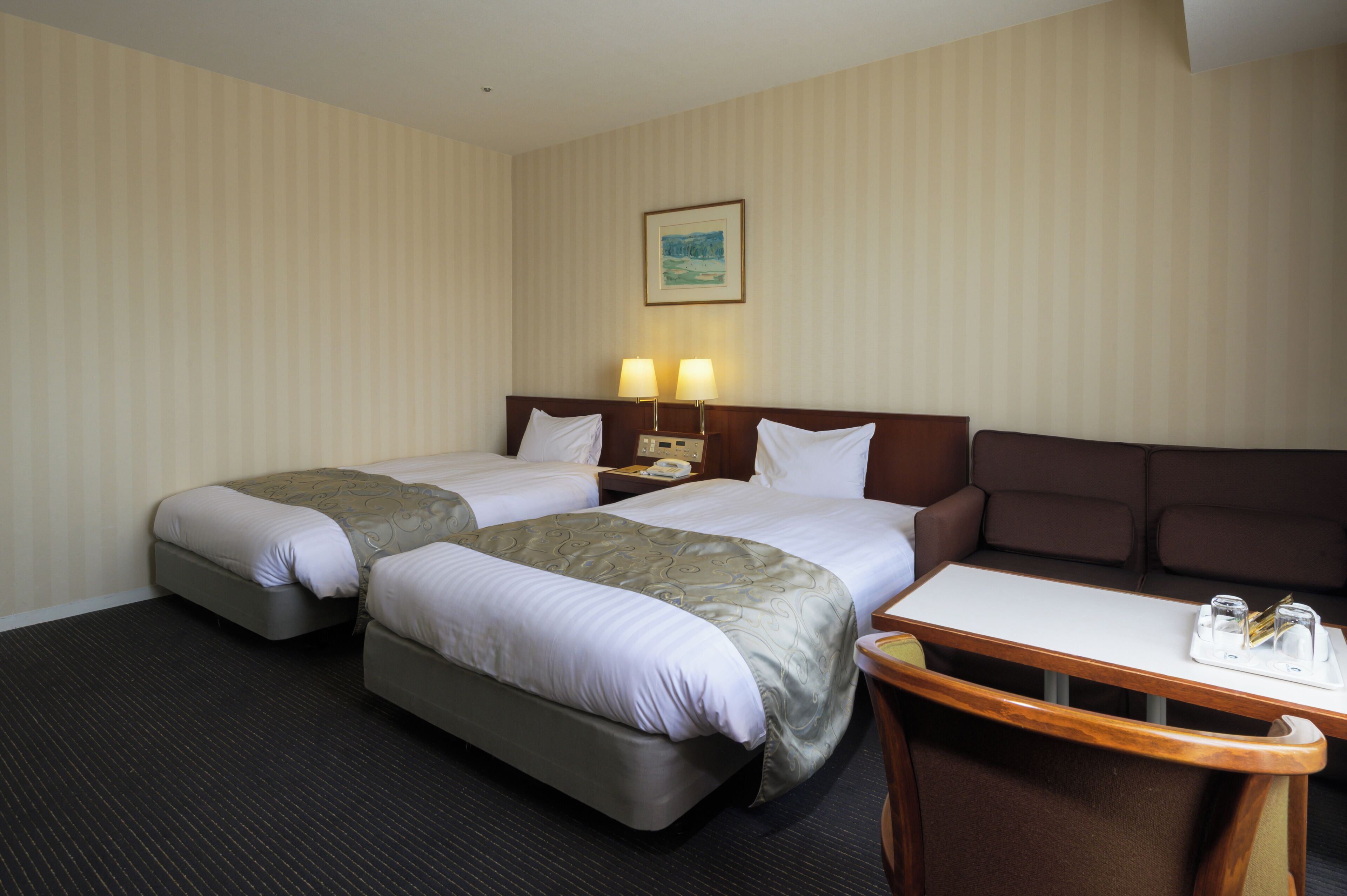 Quarto de hotel com duas camas, uma mesinha com bandeja e um sofá.