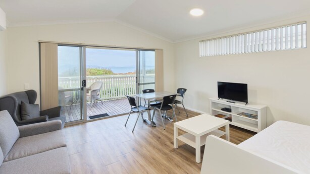A modern hotel room with a balcony, a TV, a dining table, and a sofa.