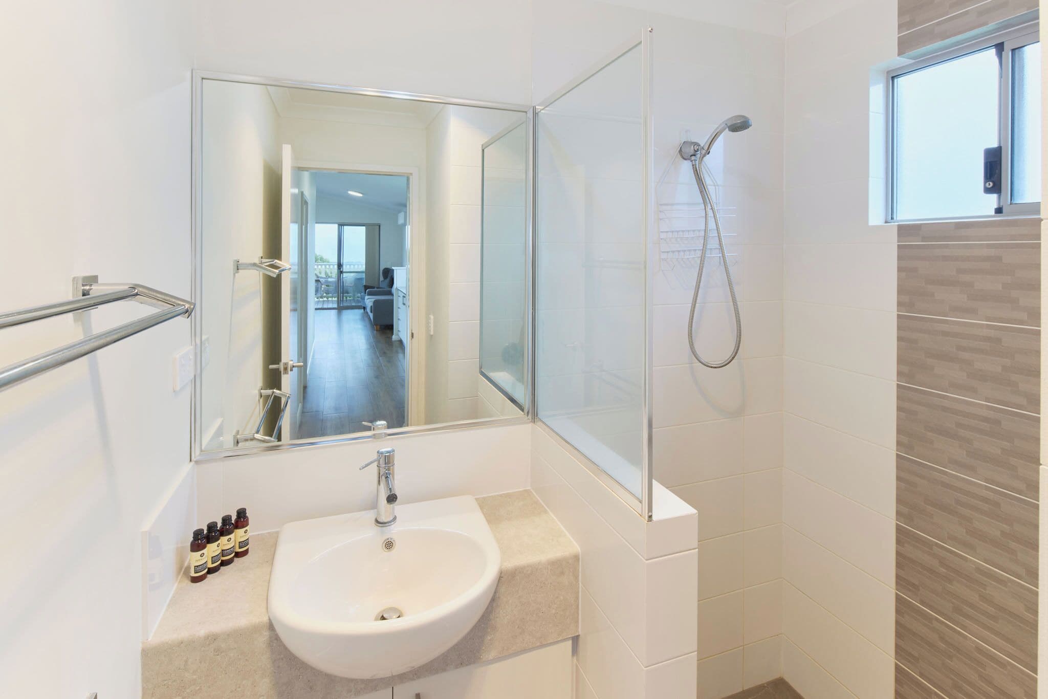 A modern bathroom with a glass shower enclosure, a sink with a mirror, and a view of the adjacent living area.