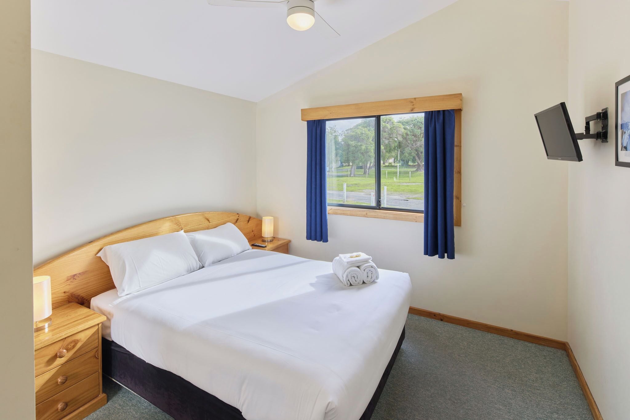 A hotel room with a bed, a nightstand, a wall-mounted TV, and a window with curtains.