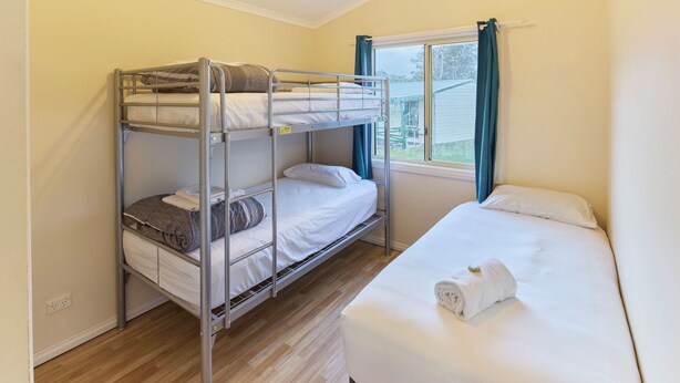 Una habitación con literas, una cama individual, una ventana con cortinas y vistas al exterior.