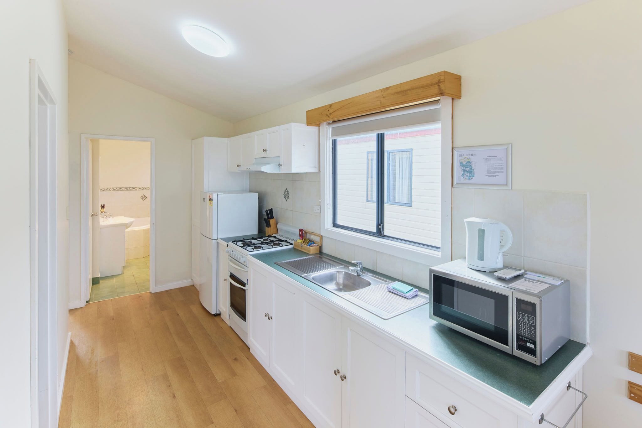 A kitchen with white cabinets, a stove, a microwave, and a window with blinds.