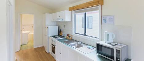 A kitchen with white cabinets, a stove, a microwave, and a window with blinds.