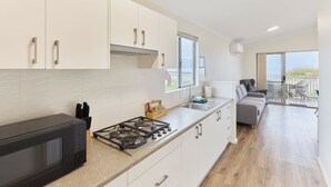 A modern kitchen with white cabinets, a gas stove, and a microwave. There is a balcony with a view.