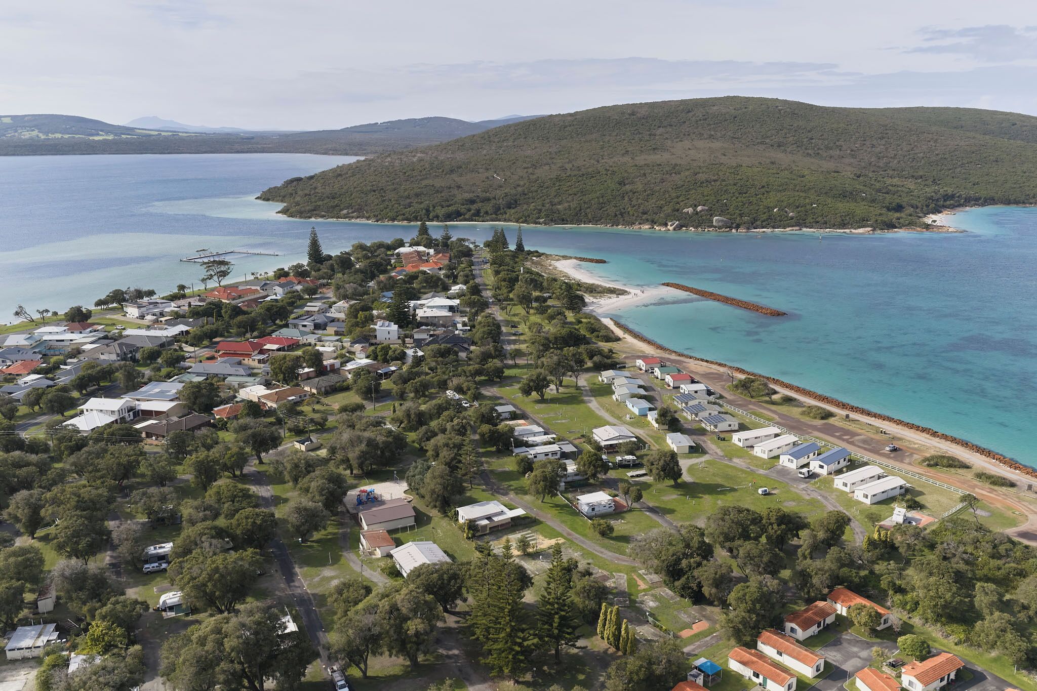 An aerial view of a coastal residential area with houses, a pier, and a beach.