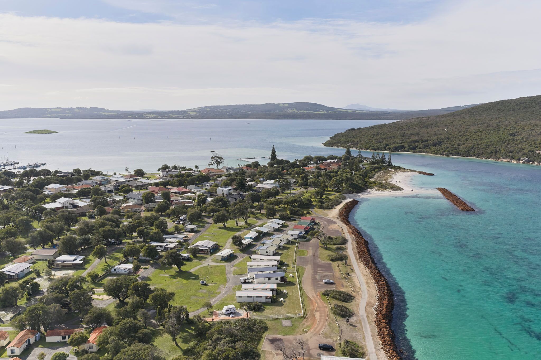 An aerial view of a coastal area with a row of houses, a beach, and a clear view of the sea.