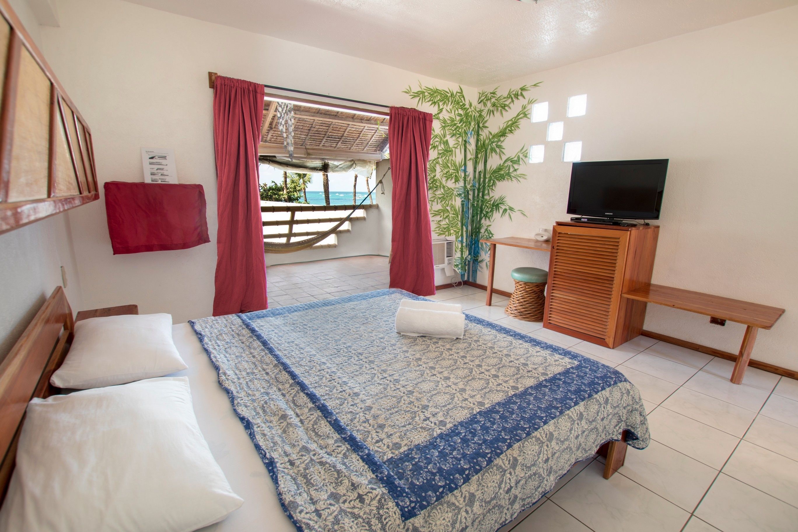 A bedroom with a bed, a TV, a bench, and a view of the outdoors.