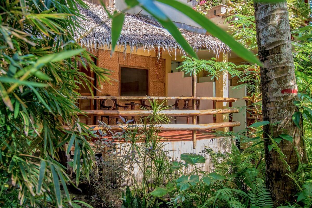 Una estructura con techo de paja y balcón de madera, rodeada de densa vegetación tropical.