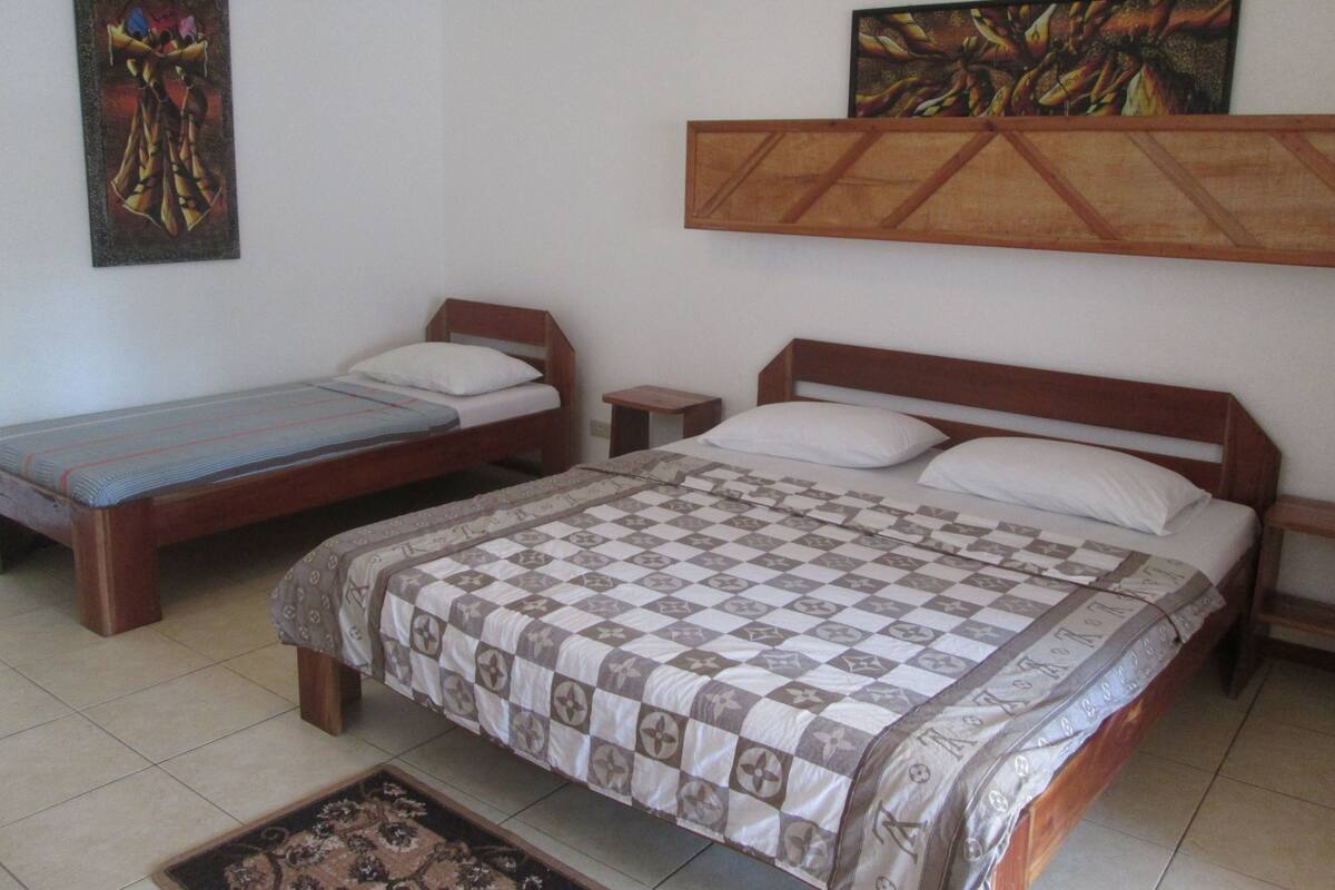 Una habitación con dos camas de madera, una mesita de noche pequeña y un estante en la pared con obras de arte.