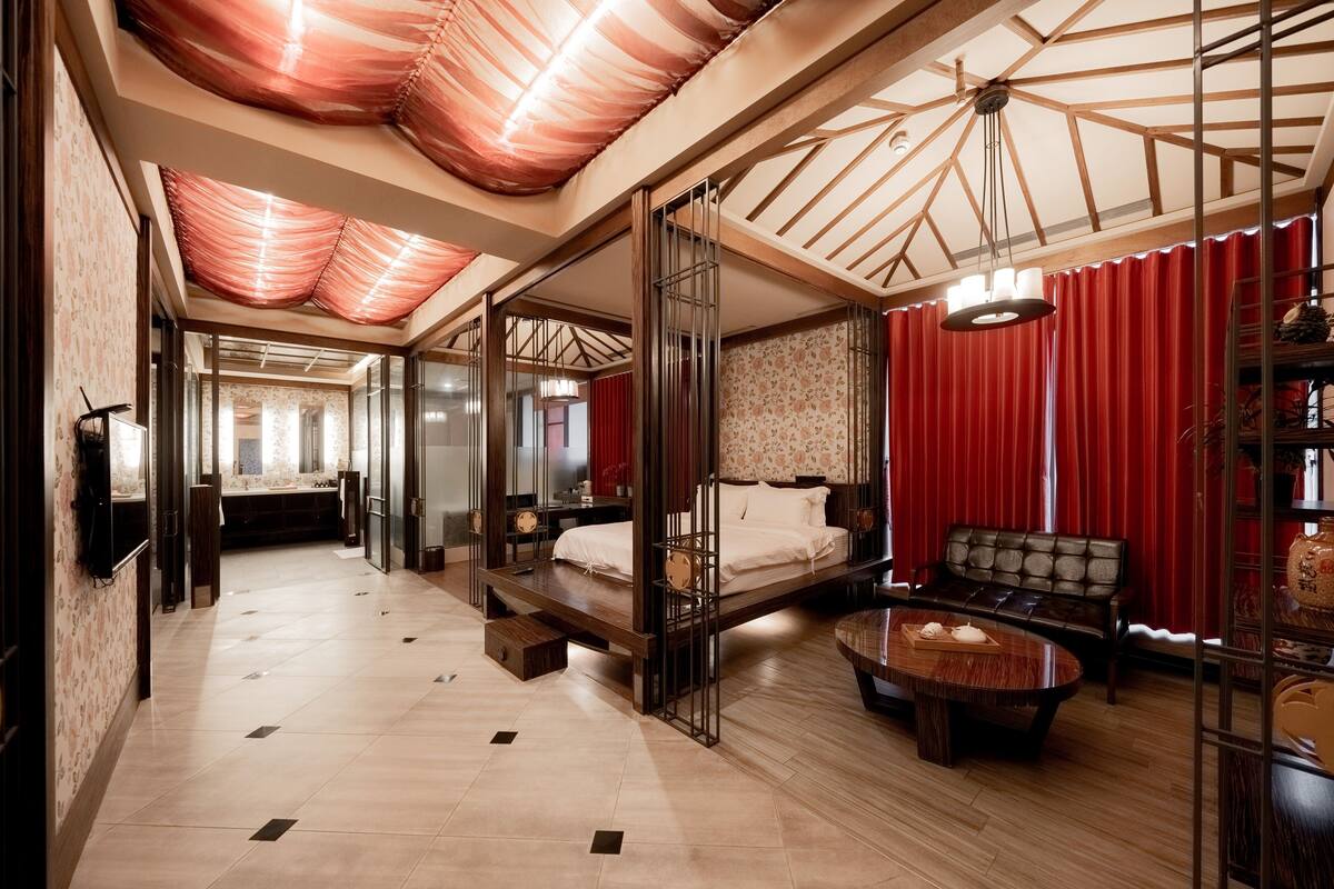A spacious hotel room with a large bed, a sofa, a coffee table, and a TV.