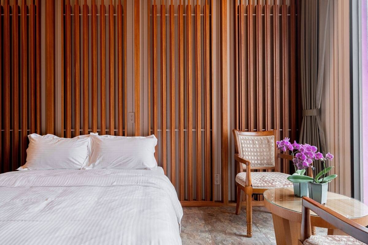 A bedroom with a bed, a chair, a small table, and a window with curtains.