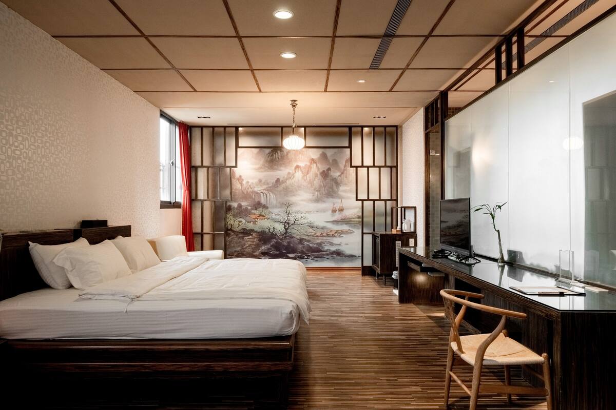 A modern bedroom with a large bed, a desk, and a TV.