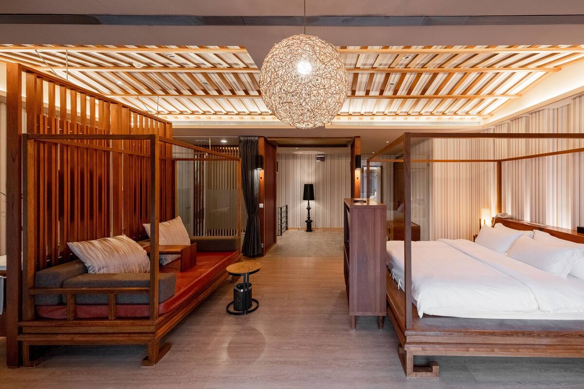 A modern hotel room with a wooden ceiling, a large bed, a seating area, and a decorative hanging light fixture.