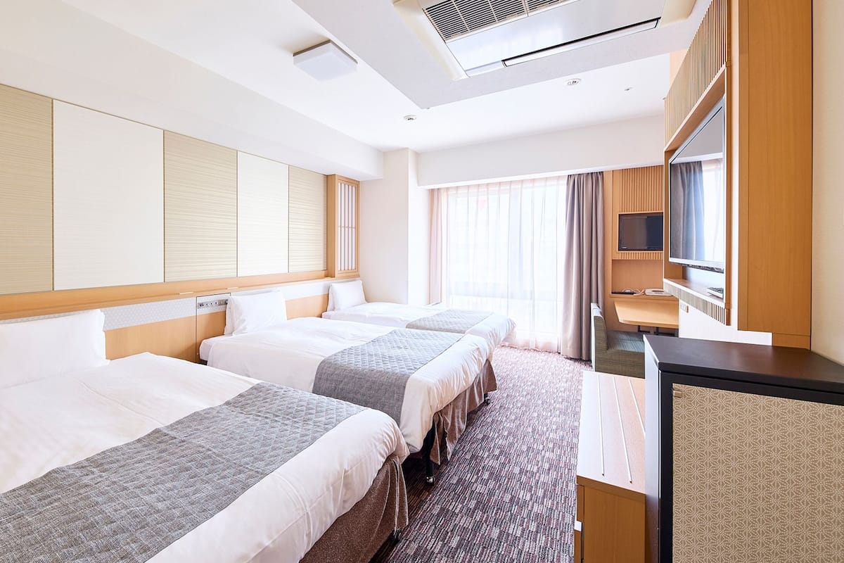 A hotel room with two beds, a desk, a TV, and a large window.