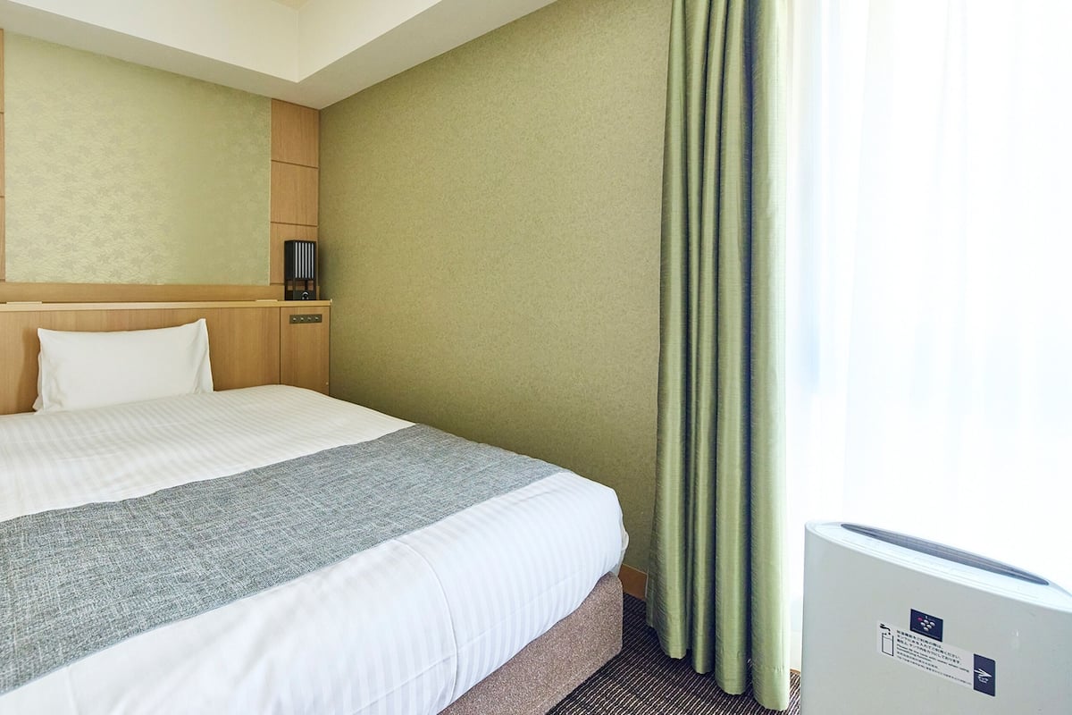 A hotel room with a bed, a headboard, a nightstand, a lamp, and a window with curtains.