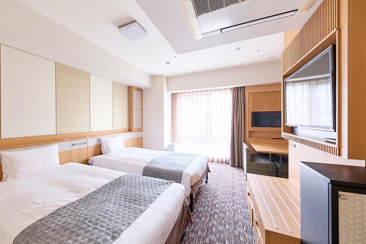 A hotel room with two beds, a desk, a TV, and a large window.