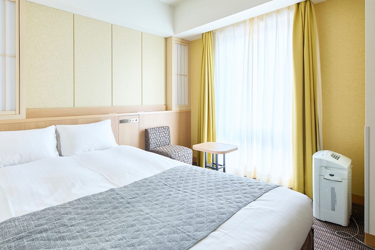 A hotel room with a large bed, a bedside table, a chair, and a window with curtains.
