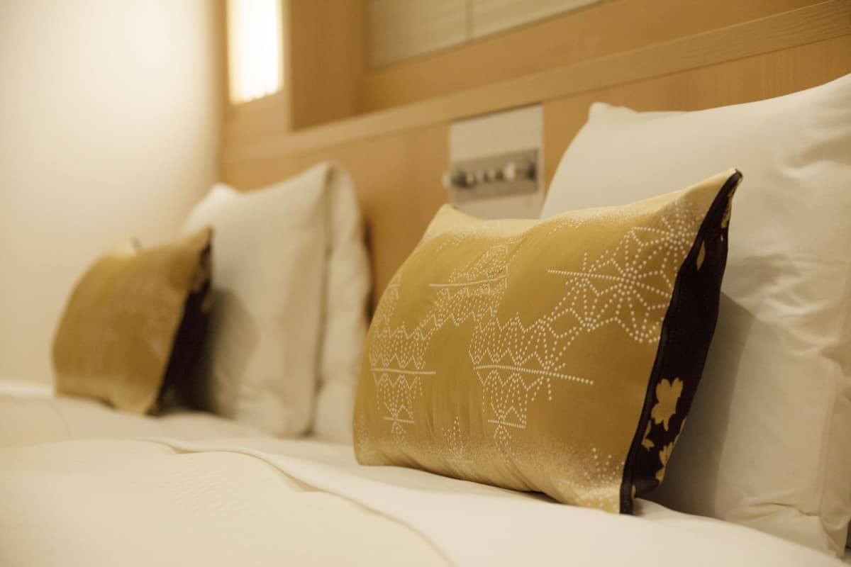 A hotel room with a neatly made bed, pillows with a geometric pattern, and a wooden headboard.