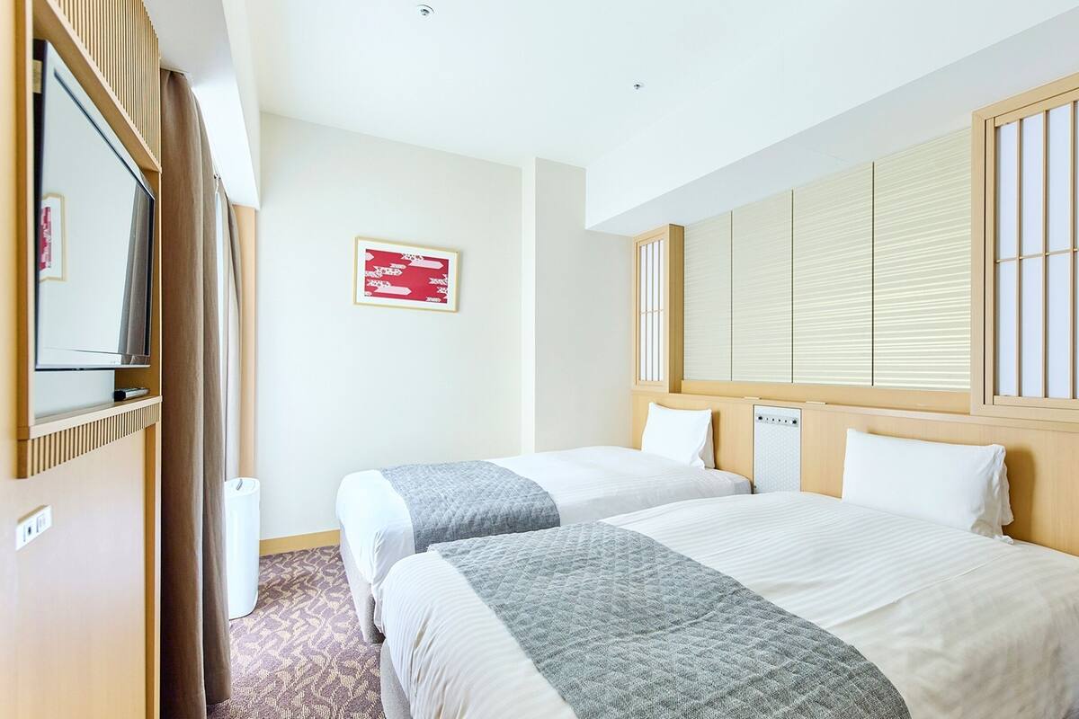 A hotel room with two beds, a TV, a window with blinds, and a red sign on the wall.