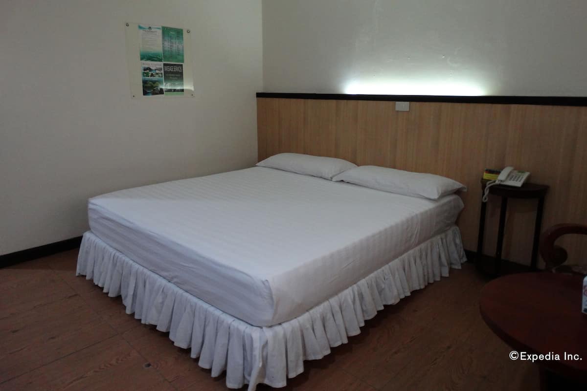 Une chambre d’hôtel avec un lit simple, une tête de lit en bois, une petite table de chevet avec un téléphone et une affiche accrochée au mur.
