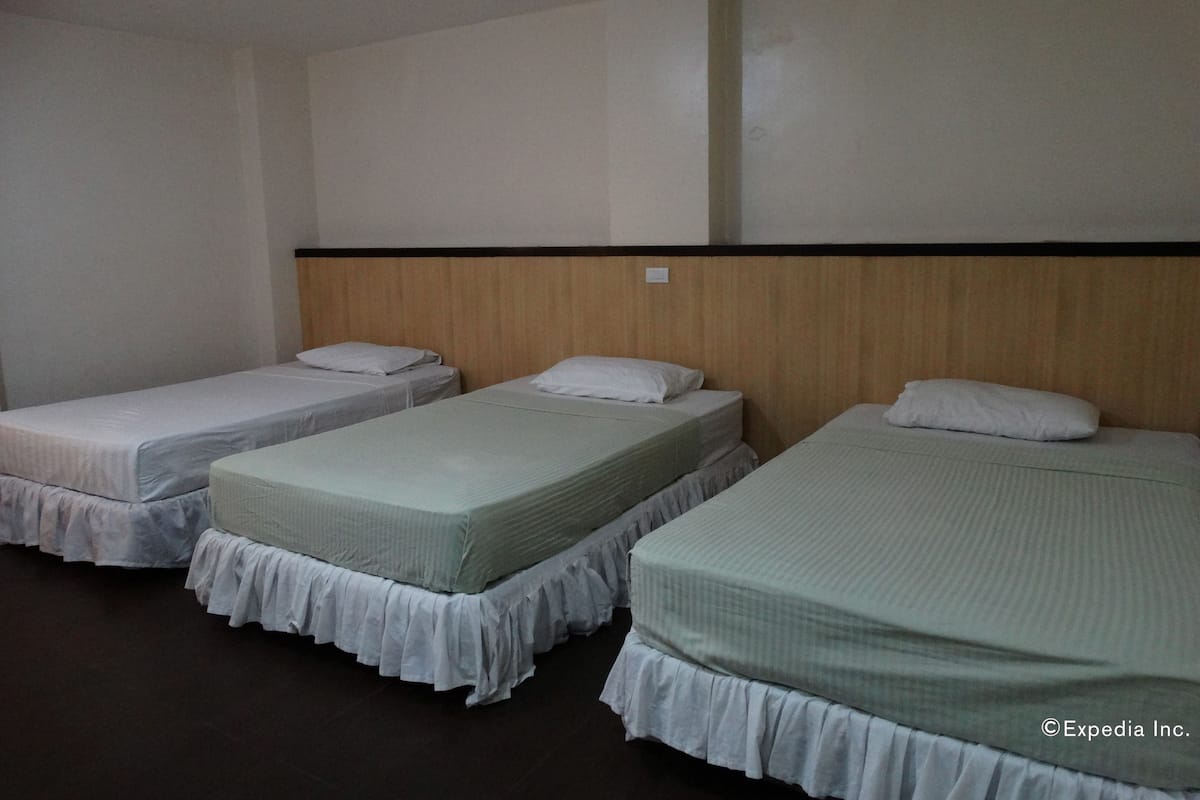Une chambre d’hôtel avec trois lits simples, chacun recouvert d’une courtepointe blanche et doté d’une tête de lit en bois.