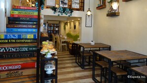 A cozy cafe with a stack of books, wooden tables, and a green booth. - Panda Tea Garden Suites (Tagbilaran)