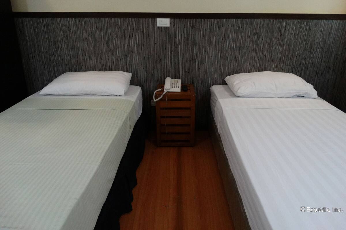 Une chambre d’hôtel avec deux lits simples, une table de chevet en bois avec un téléphone et un mur à motifs.