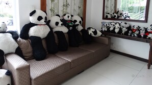 A room with a sofa displaying multiple panda plush toys, a mirror, and a bamboo-themed curtain. - Panda Tea Garden Suites (Tagbilaran)