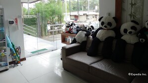 A room with a sofa, a glass door leading outside, and several panda plush toys. - Panda Tea Garden Suites (Tagbilaran)