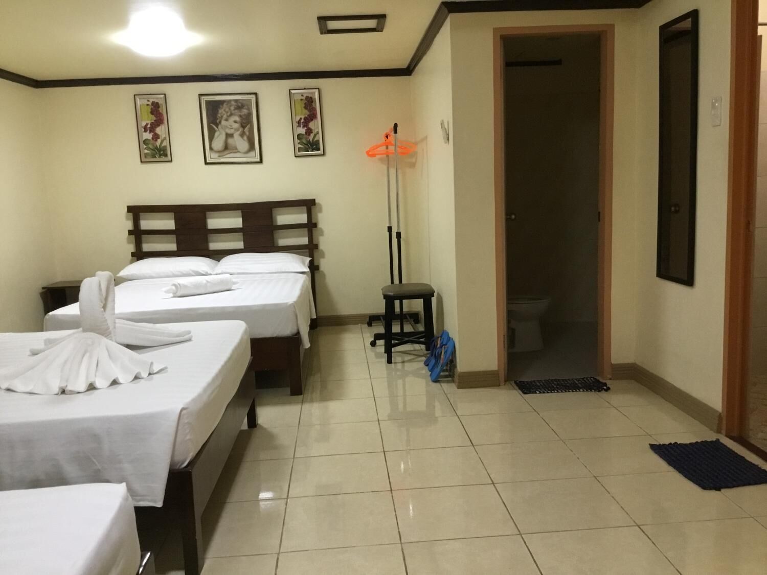 Habitación de hotel con tres camas, cabecera de madera, lámpara de pie y puerta que da al baño.