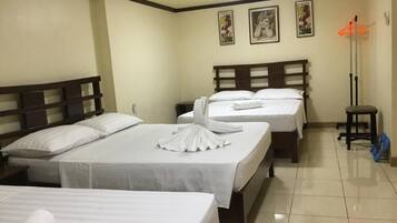 A hotel room with three beds, each with white linens and towels, a wooden headboard, and a small stool.