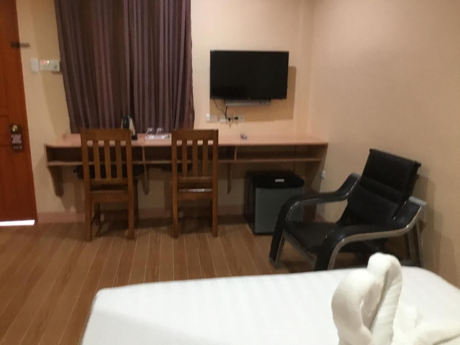 A hotel room with a bed, a desk with two chairs, a television, and a trash bin.