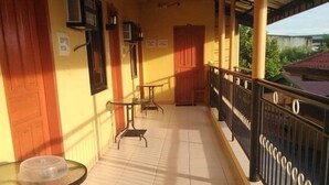 Un balcone coperto con pavimento piastrellato, un tavolo in vetro e un ringhiera metallica.