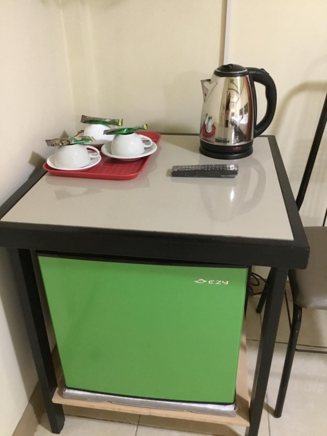 A small kitchenette with a green refrigerator, a coffee maker, a kettle, and a remote control on a table.