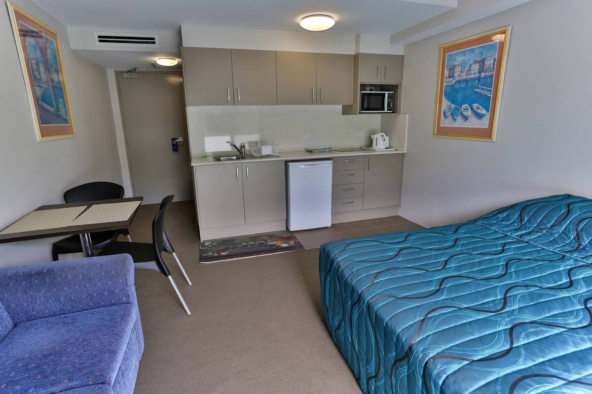 A compact hotel room with a kitchenette, a single bed, a small table, and a chair.