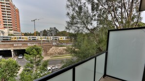 A balcony with a view of a train passing under a bridge, a road with vehicles, and a construction site. - Strathfield Executive Accommodation (Strathfield)