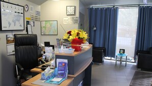 A hotel reception area with a desk, chairs, a clock, and informational posters on the walls. - Strathfield Executive Accommodation (Strathfield)