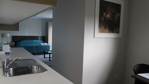 A modern hotel room with a kitchenette, a bed with teal bedding, and a framed painting on the wall. - Strathfield Executive Accommodation (Strathfield)