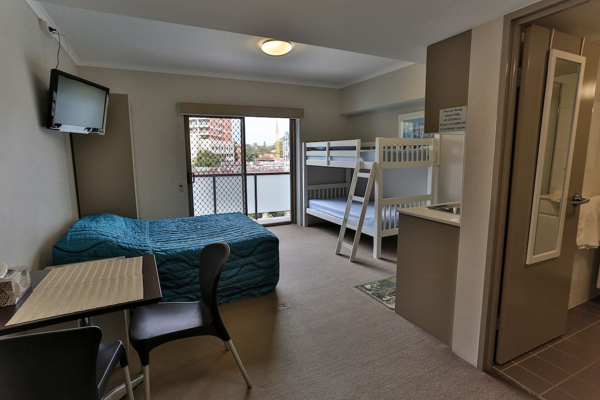 A compact room with a bed, a desk, a chair, a bunk bed, and a television.