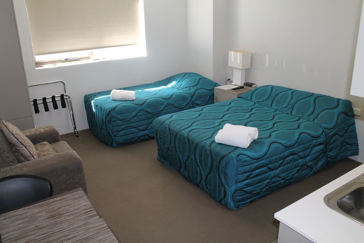 A hotel room with two beds, a sofa, a small table, a lamp, and a window with blinds.