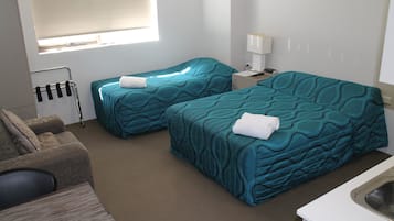 A hotel room with two beds, a sofa, a small table, a lamp, and a window with blinds.