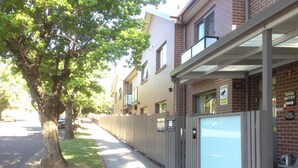 A street view with a sidewalk, a tree-lined street, and a building with a metal awning. - Strathfield Executive Accommodation (Strathfield)