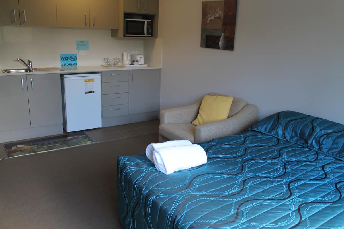 A compact hotel room with a bed, a chair, a small kitchenette, and a microwave.