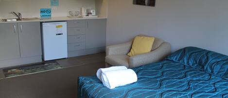 A compact hotel room with a bed, a chair, a small kitchenette, and a microwave.