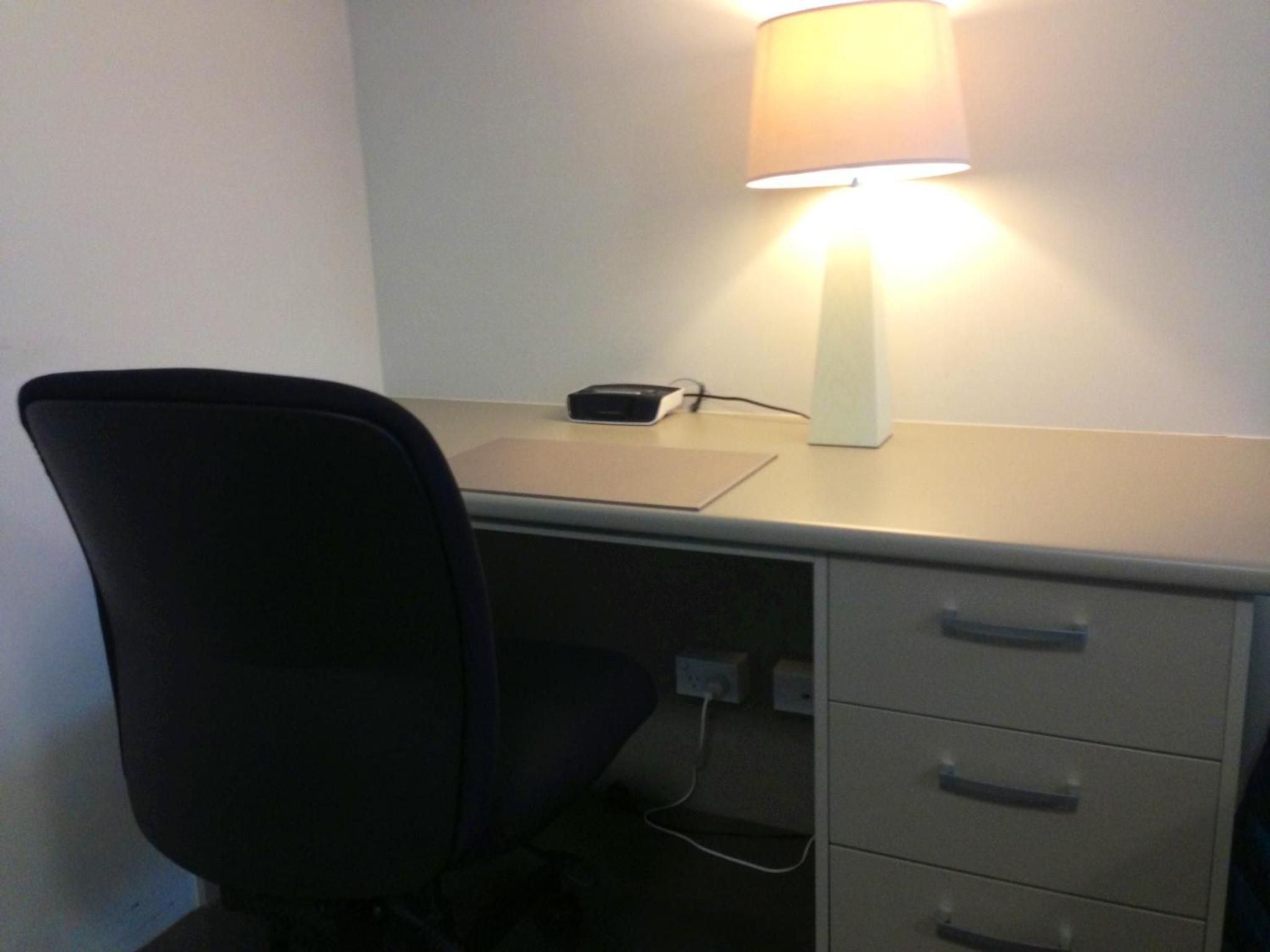 Un bureau avec une lampe, une chaise et un meuble à tiroirs.