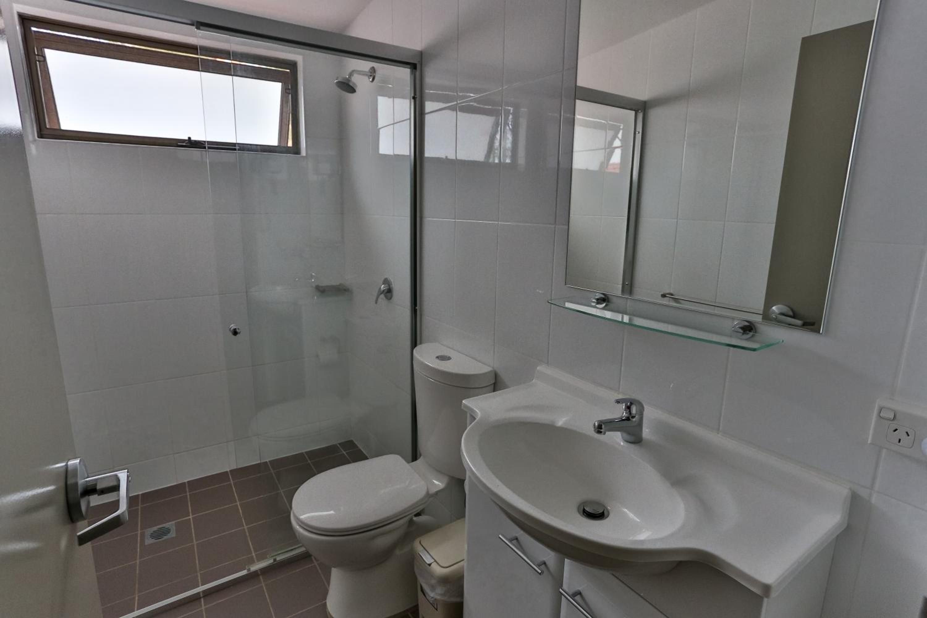 A bathroom with a glass-enclosed shower, a toilet, a sink, and a mirror.