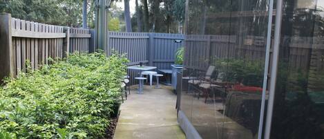 A patio area with a wooden fence, green bushes, and outdoor furniture.