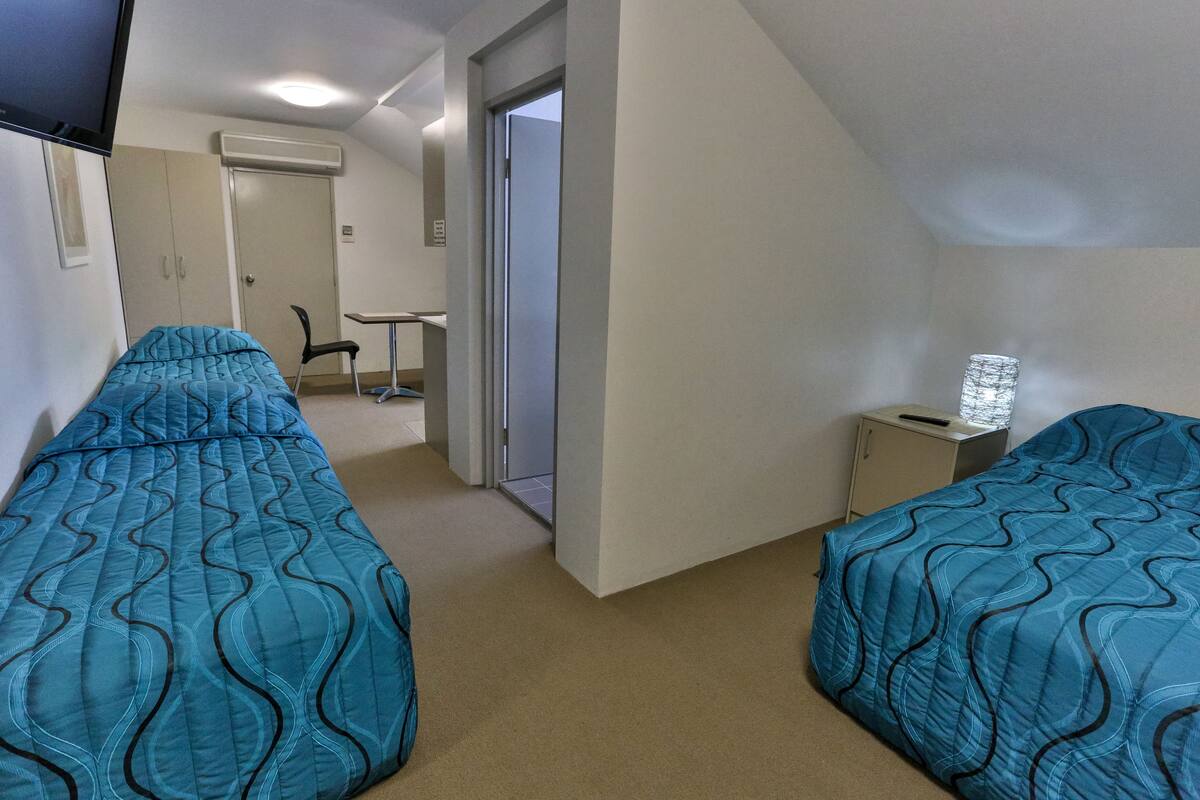 A room with two beds, a desk, a chair, and a small cabinet.