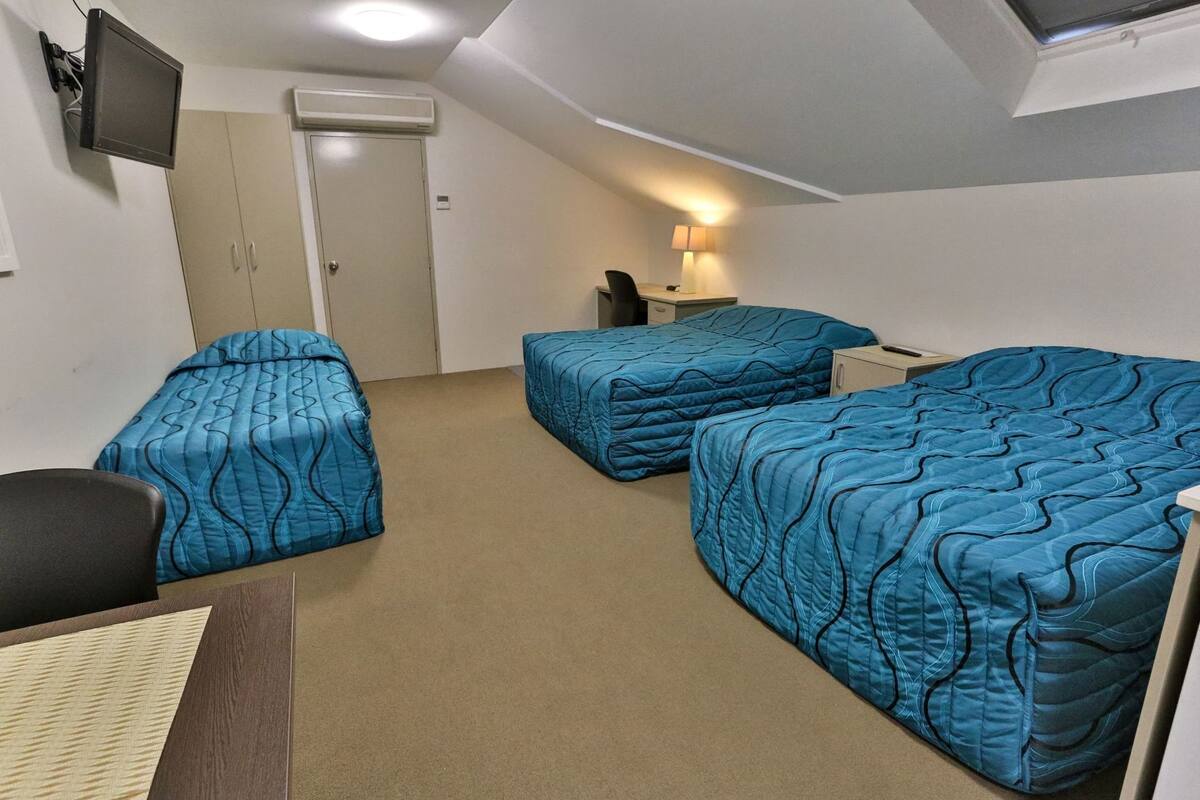 A room with three beds, a desk, a chair, a TV, and a lamp.